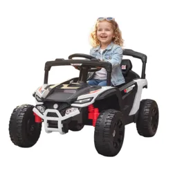 A child is driving a black and white toy ride-on car down a cobblestone path surrounded by vibrant flowers in a garden setting.