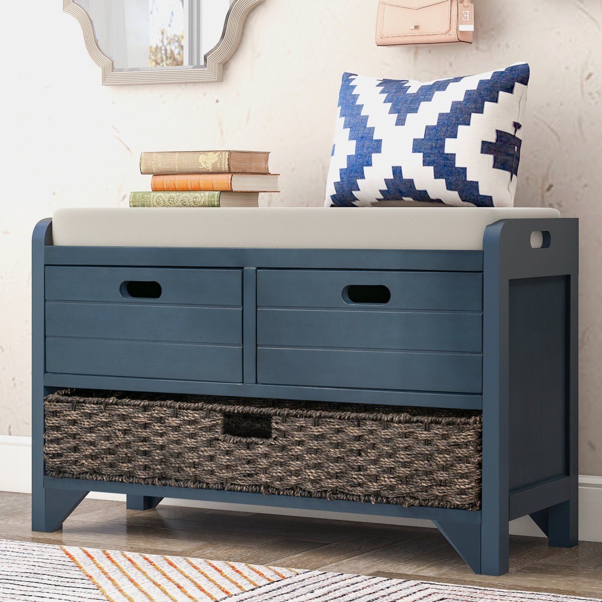 Blue storage bench with a cushioned seat, featuring two upper drawers and a woven basket in the lower section. A blue-white patterned pillow and stacked books are on top.