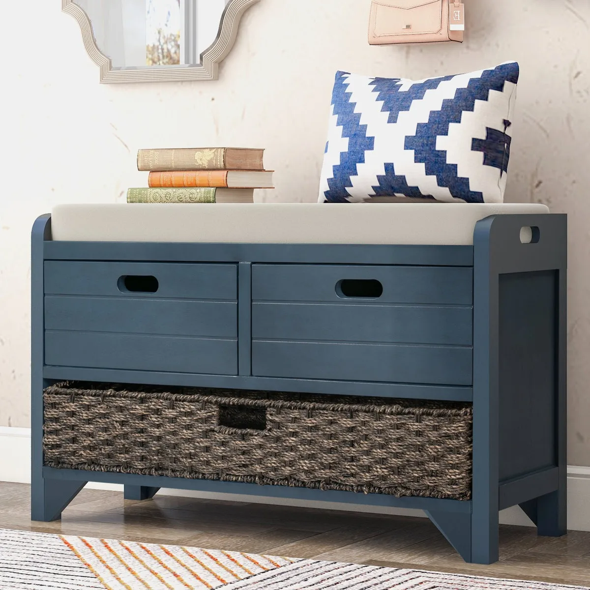 Blue storage bench with a cushioned seat, featuring two upper drawers and a woven basket in the lower section. A blue-white patterned pillow and stacked books are on top.