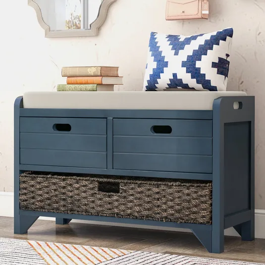 Blue storage bench with a cushioned seat, featuring two upper drawers and a woven basket in the lower section. A blue-white patterned pillow and stacked books are on top.