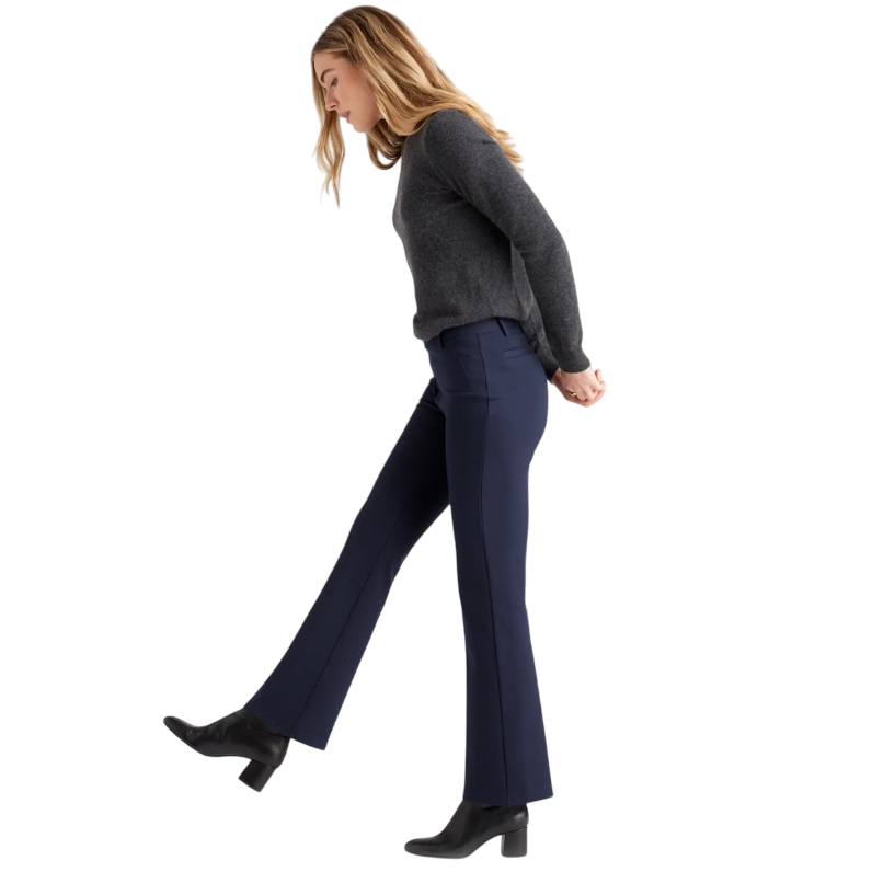 A woman is wearing a grey sweater, navy flared trousers, and black heeled boots.