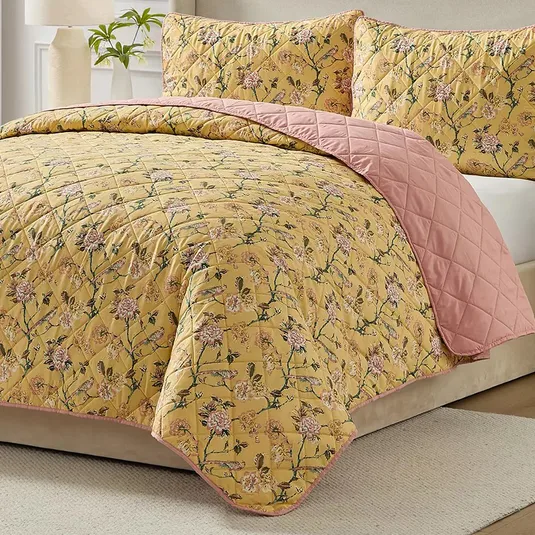 A quilt set with a floral pattern on a yellow background and a reversible pink backing, displayed with matching pillow shams on a bed.