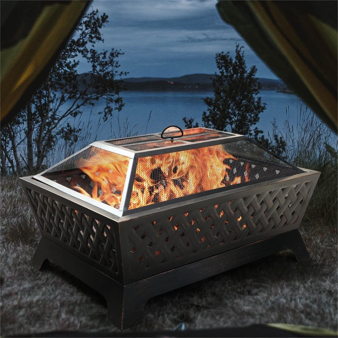 A metal fire pit with a protective mesh lid, set outdoors against a dusk sky.