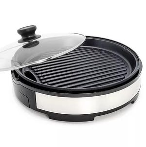 Round electric grill with a ribbed cooking surface and a transparent lid featuring a black handle.