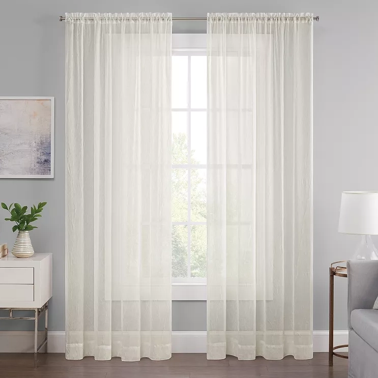 Light, translucent white sheer curtains hang from a curtain rod, gently diffusing the light from a window in a room with modern decor.