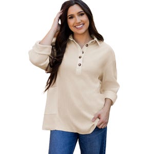 Beige women's waffle knit top with long sleeves and a collar, featuring a button-down front placket and pockets. Paired with blue jeans.