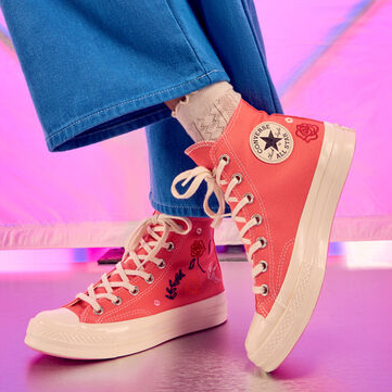 A person is wearing pink high-top sneakers with lace-up fronts and visible branding on the ankle patch.