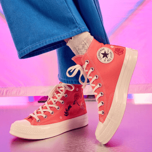 A person is wearing pink high-top sneakers with lace-up fronts and visible branding on the ankle patch.