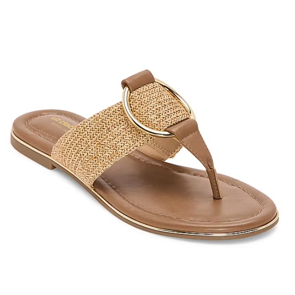 Brown thong sandal with a flat sole features a wide woven strap with a large gold circular buckle accent. Designed for casual wear.