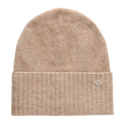 A beige knit beanie with a folded brim featuring a small circular logo, likely made from soft material for warmth.