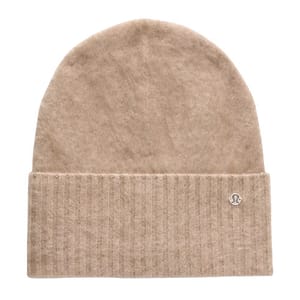 A beige knit beanie with a folded brim featuring a small circular logo, likely made from soft material for warmth.