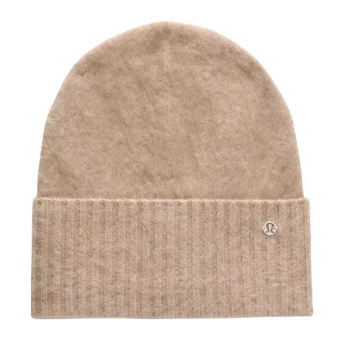 A beige knit beanie with a folded brim featuring a small circular logo, likely made from soft material for warmth.
