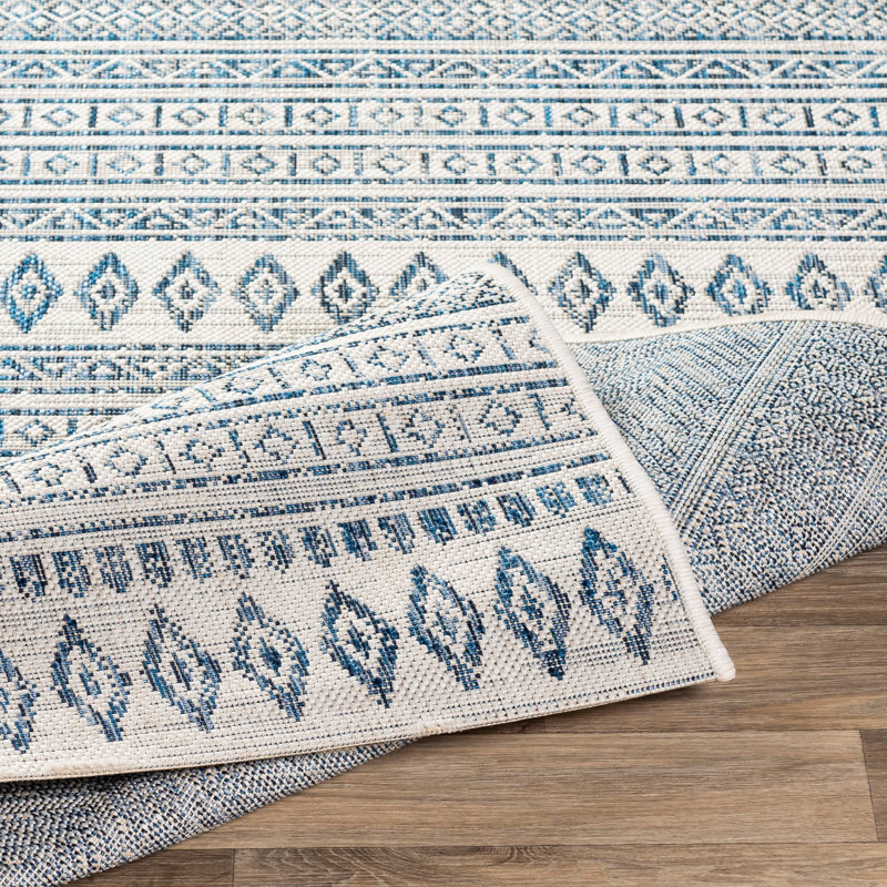 A woven rug featuring geometric patterns in shades of blue and white is partially rolled on a wooden floor.