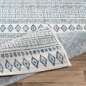 A woven rug featuring geometric patterns in shades of blue and white is partially rolled on a wooden floor.