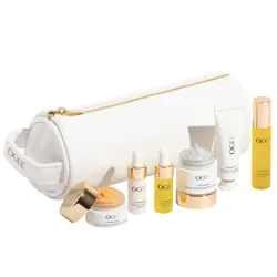 A white cosmetic bag with gold zipper contains Ogee skincare items: Indigo Dream Renewal Cream, Brightening Botanical Gel, Seeds of Youth Serum, Jojoba Glow Face Oil, and Liquid Gold Cleansing Oil, each in small containers and tubes.