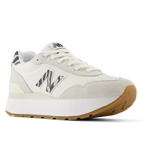 New Balance Women's Classic Sneakers feature a white and cream color scheme with a distinctive striped logo, suede overlays, a mesh upper, and a gum rubber sole. They offer a sporty yet stylish look with a comfortable, elevated platform design.