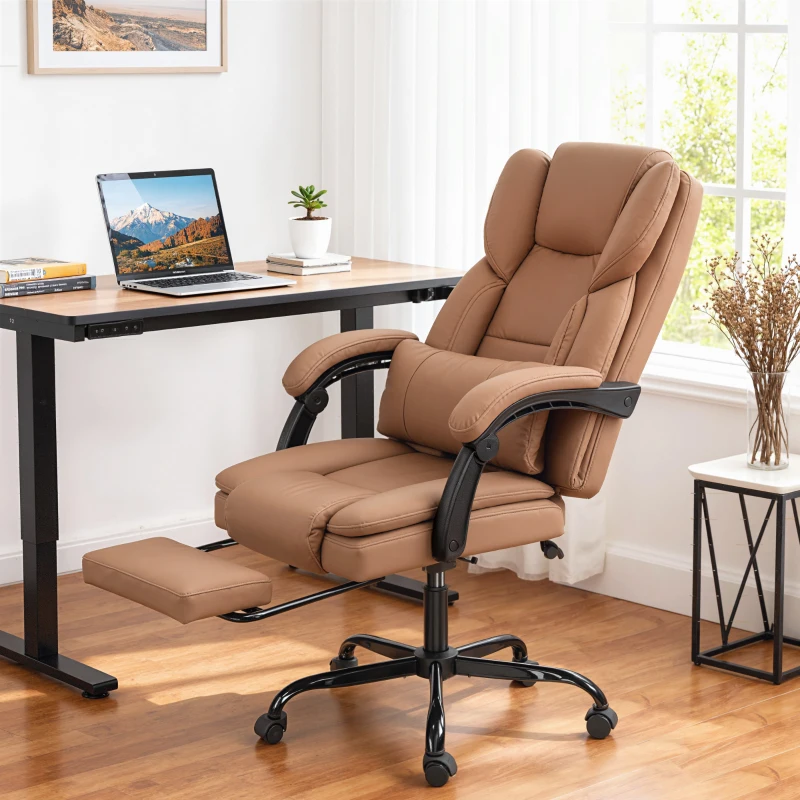 A tan ergonomic office chair with cushioned armrests and a retractable footrest is positioned next to a desk with a laptop, books, and a small plant on its surface.