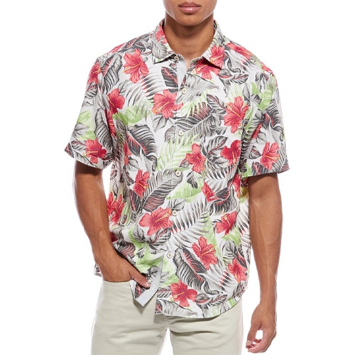 A short-sleeve button-up Hawaiian shirt featuring a vibrant floral pattern with red flowers and green leaves on a light background, paired with beige pants.