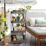 A four-tier, gray utility cart with wheels is stocked with plant pots, books, and pantry items, positioned next to an outdoor lounge area.