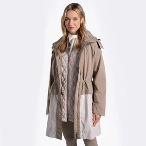 A woman modeling a layered beige raincoat with quilted lining and hood.