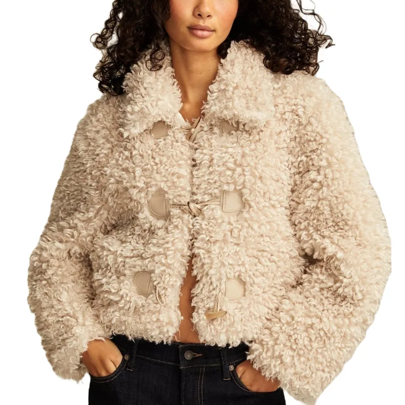 A short, cream-colored faux teddy jacket with a toggle-style closure and a plush, curly texture. It features a collar and long sleeves, paired with dark jeans.