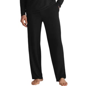 Black pajama pants with a relaxed fit, featuring side pockets and an elastic waistband. The person wearing them is barefoot.