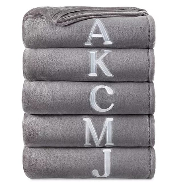 A stack of four gray, monogrammed towels with the letters A, K, C, and J embroidered in white.