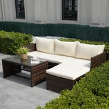 Outdoor patio set with an L-shaped cushioned sofa in beige and a glass-top coffee table, both made from dark brown wicker.