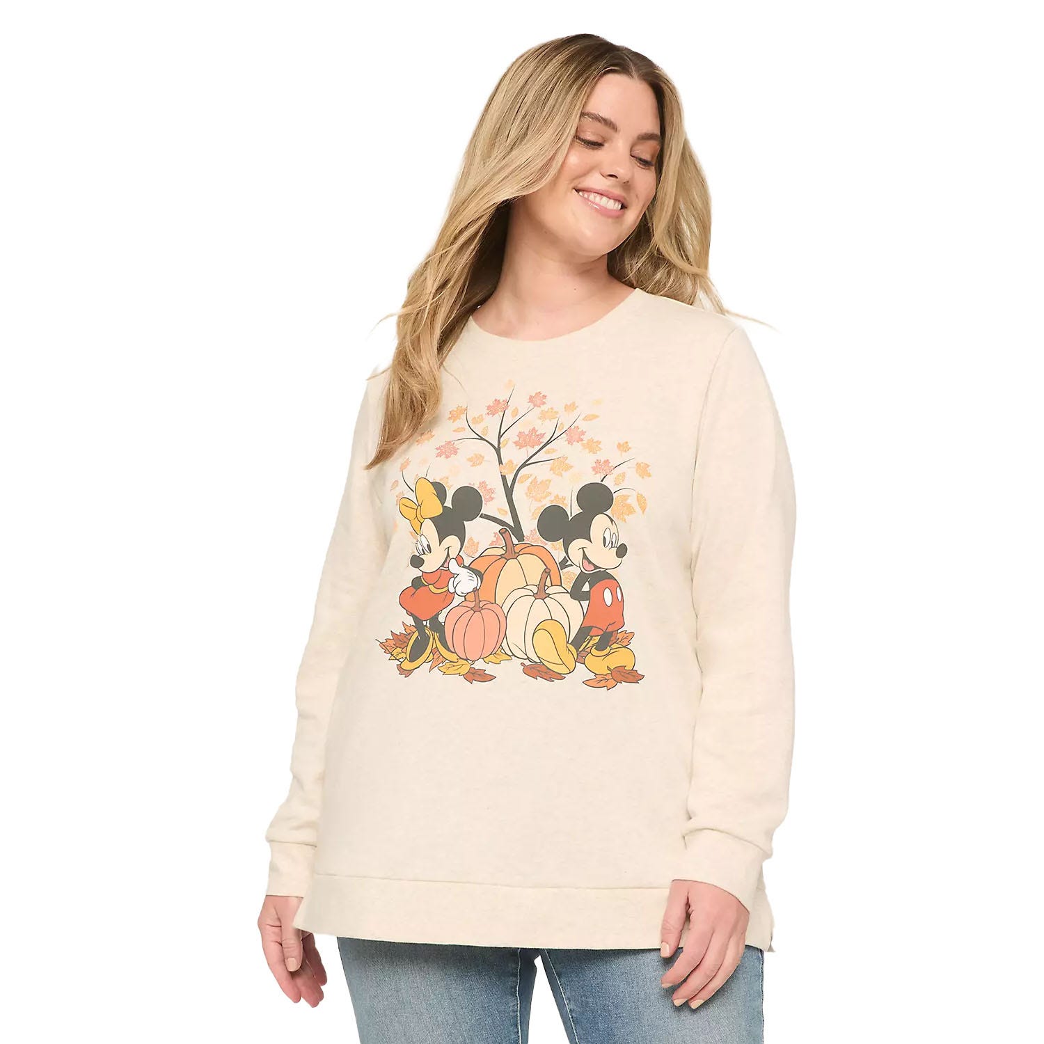 A woman wearing a cream-colored sweatshirt featuring Mickey and Minnie Mouse surrounded by pumpkins and autumn leaves, paired with blue jeans.