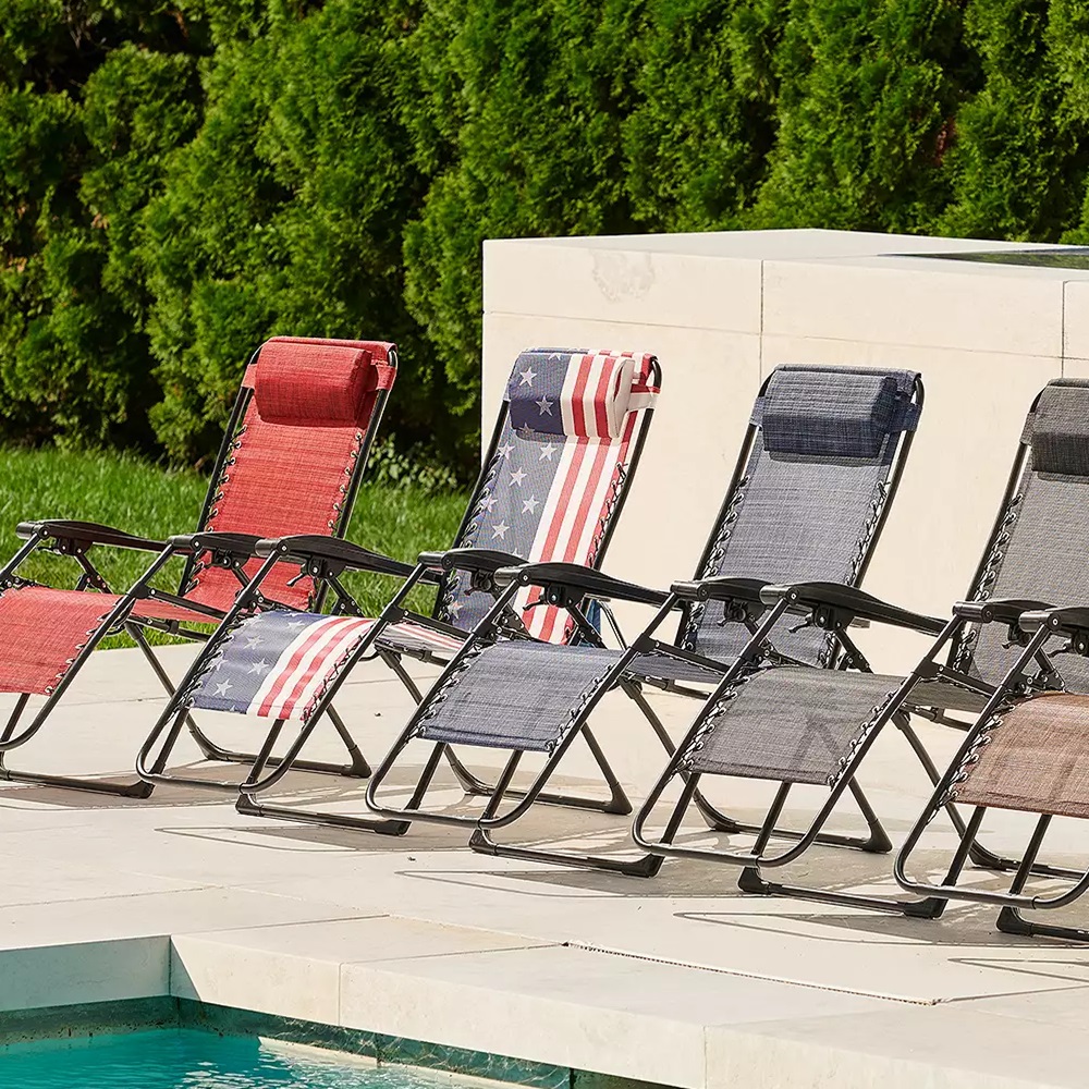 Six folding lounge chairs by a poolside, varying in colors and one with an American flag design.