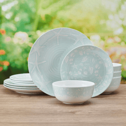 A set of pastel blue dishware with sea-themed patterns, including starfish, consists of plates, bowls, and smaller saucers, displayed on a wooden surface with a blurred garden background.