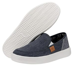A pair of denim slip-on shoes with a thick white sole and a small logo tag on the side.