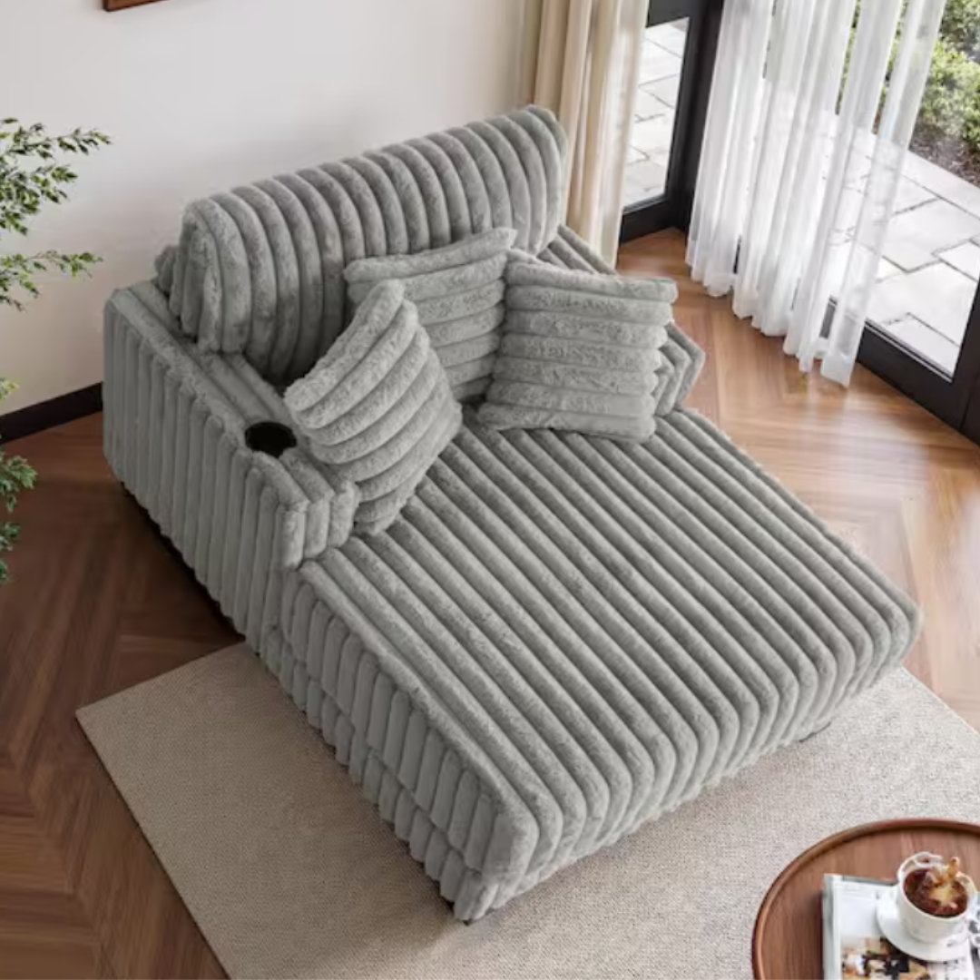 Gray, ribbed chaise lounge with matching throw pillows, cup holder, and positioned on a neutral rug by a window.
