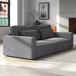 A gray corduroy sofa with an extra-deep design, featuring wide armrests and layered cushions for added comfort. The sofa is set in a modern living room with a neutral color palette and large windows.