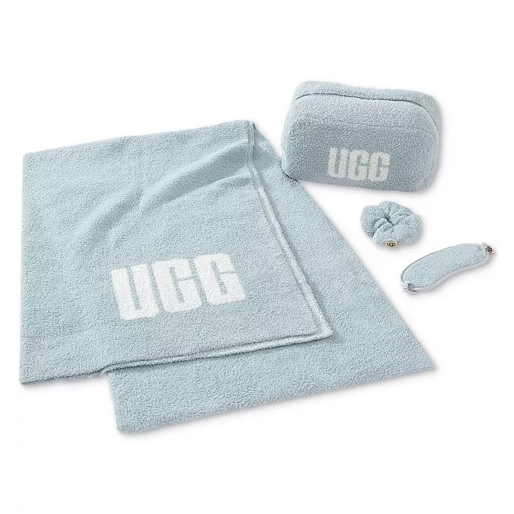 Light blue 4-piece UGG travel set includes a throw blanket, a zip-up pouch, a scrunchie, and a sleep mask, each featuring the UGG logo.