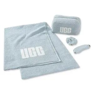 Light blue 4-piece UGG travel set includes a throw blanket, a zip-up pouch, a scrunchie, and a sleep mask, each featuring the UGG logo.