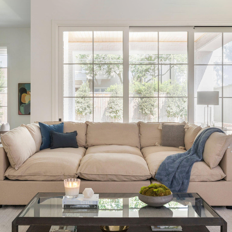 Large beige sectional sofa with throw pillows and blankets, glass coffee table with decorative items.