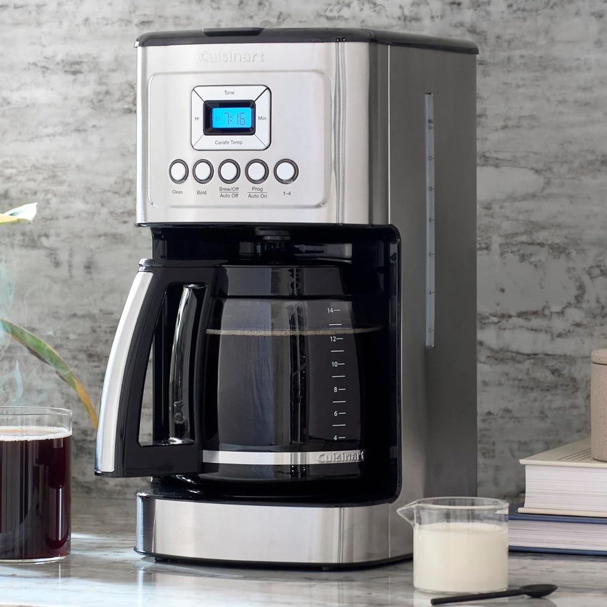 A Cuisinart coffee maker with a digital display, alongside a glass mug with coffee and a measuring jug with milk.