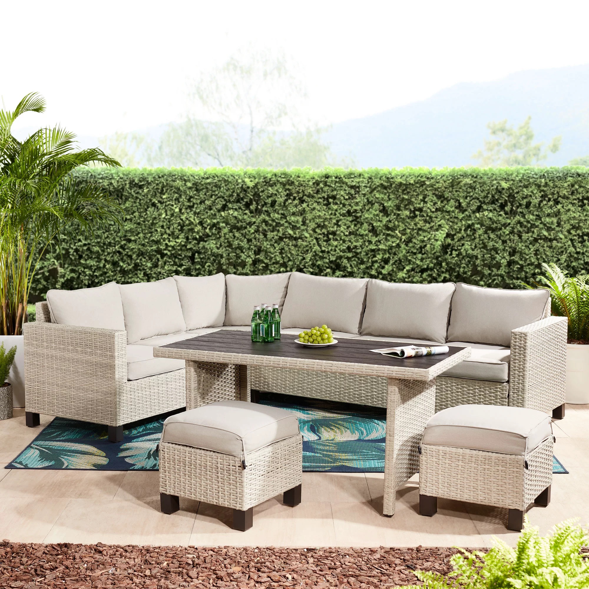 Outdoor patio furniture set with a sofa, two chairs, a table, and an ottoman, all with matching wicker design and beige cushions.