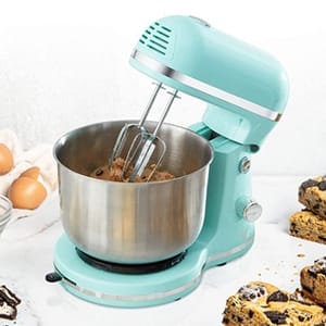 A teal stand mixer with a stainless-steel bowl and whisk attachment, surrounded by eggs and cookie ingredients.