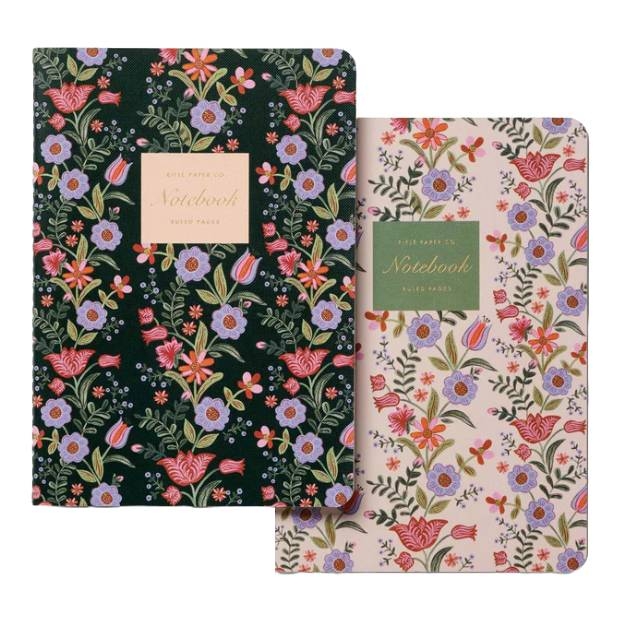 Two notebooks feature vibrant floral designs, one with a dark background and the other with a light background. Both have decorative text labels on the front.