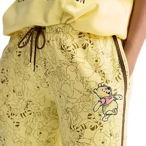 Yellow sweatpants with a drawstring and a pattern featuring a bear and friends, with a larger embroidered bear on the side.