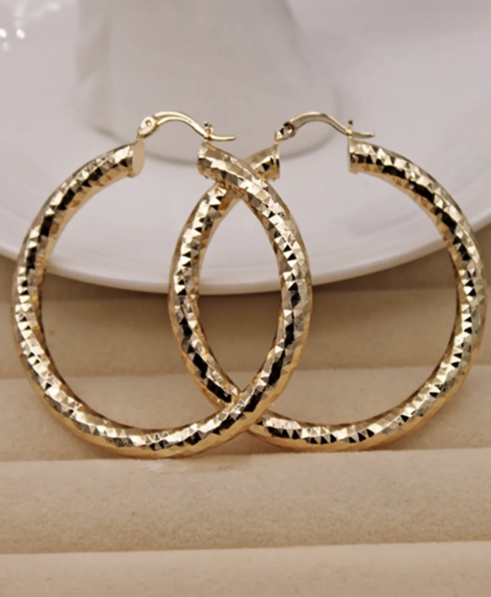 A pair of large, textured hoop earrings in gold color, displayed against a neutral background.