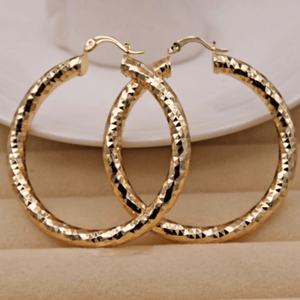A pair of large, textured hoop earrings in gold color, displayed against a neutral background.