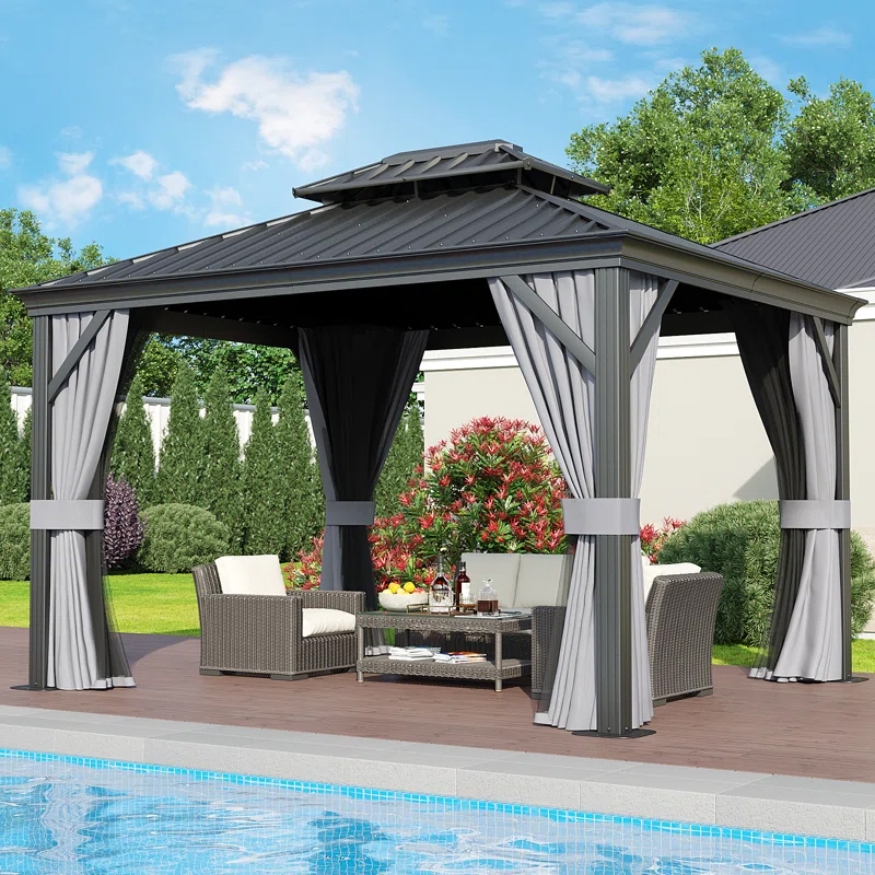 12' x 10' metal gazebo with a dark roof, light and dark curtains, placed on a poolside deck. Contains wicker furniture including cushioned chairs and a coffee table, surrounded by bushes and trees.