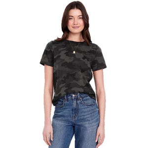 A woman wearing a dark camouflage-patterned T-shirt and blue high-waisted jeans. She has a necklace with a small square pendant.