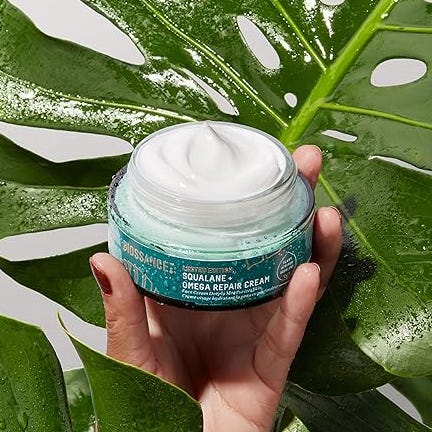 Open jar of cream held above a large green leaf.