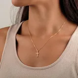 A gold chain necklace featuring a simple cross pendant is displayed against a ribbed, beige tank top.