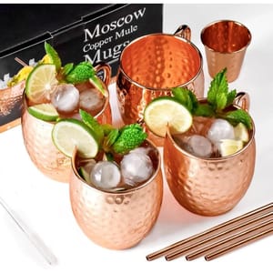 Copper mugs set for Moscow Mule drinks, featuring four polished hammered cups, garnished with lime, mint, and ice. Set includes matching copper straws and a shot glass.