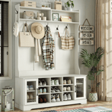 Entryway storage unit with shelves, hooks, and cubbies for shoes. Features hats, bags, a plaid shirt, and decor items like candles and plants. A sign reads \“Welcome to Our Home,\“ and there's a lantern and potted plant nearby.